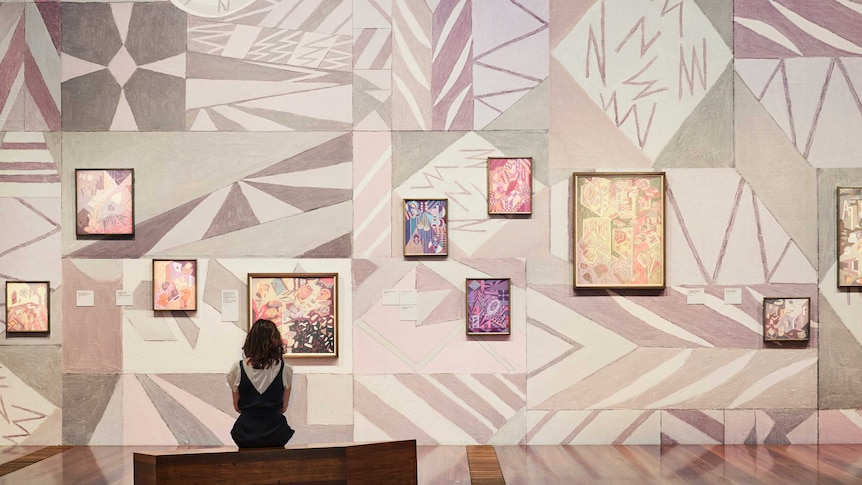A young woman sits in front of a wall of art.