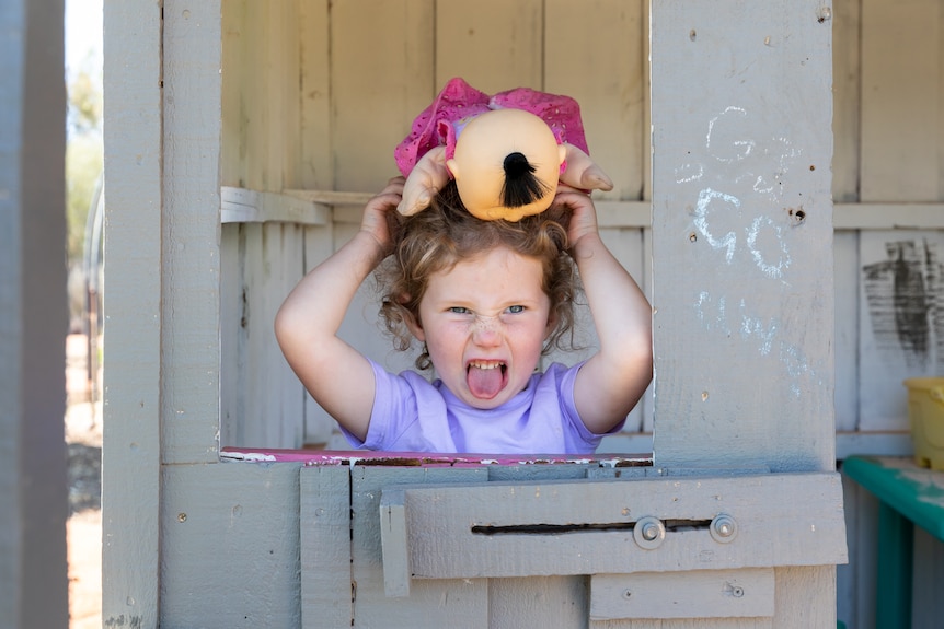 Hayley pulls a funny face and pokes her tongue out while in the cubby house. 