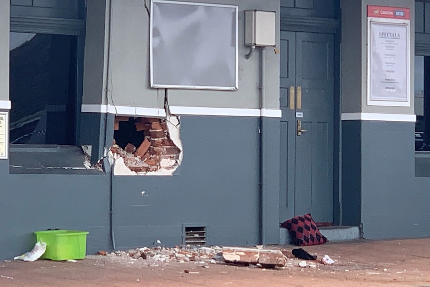 A hole smashed into the wall of a grey hotel. Red bricks have been exposed.