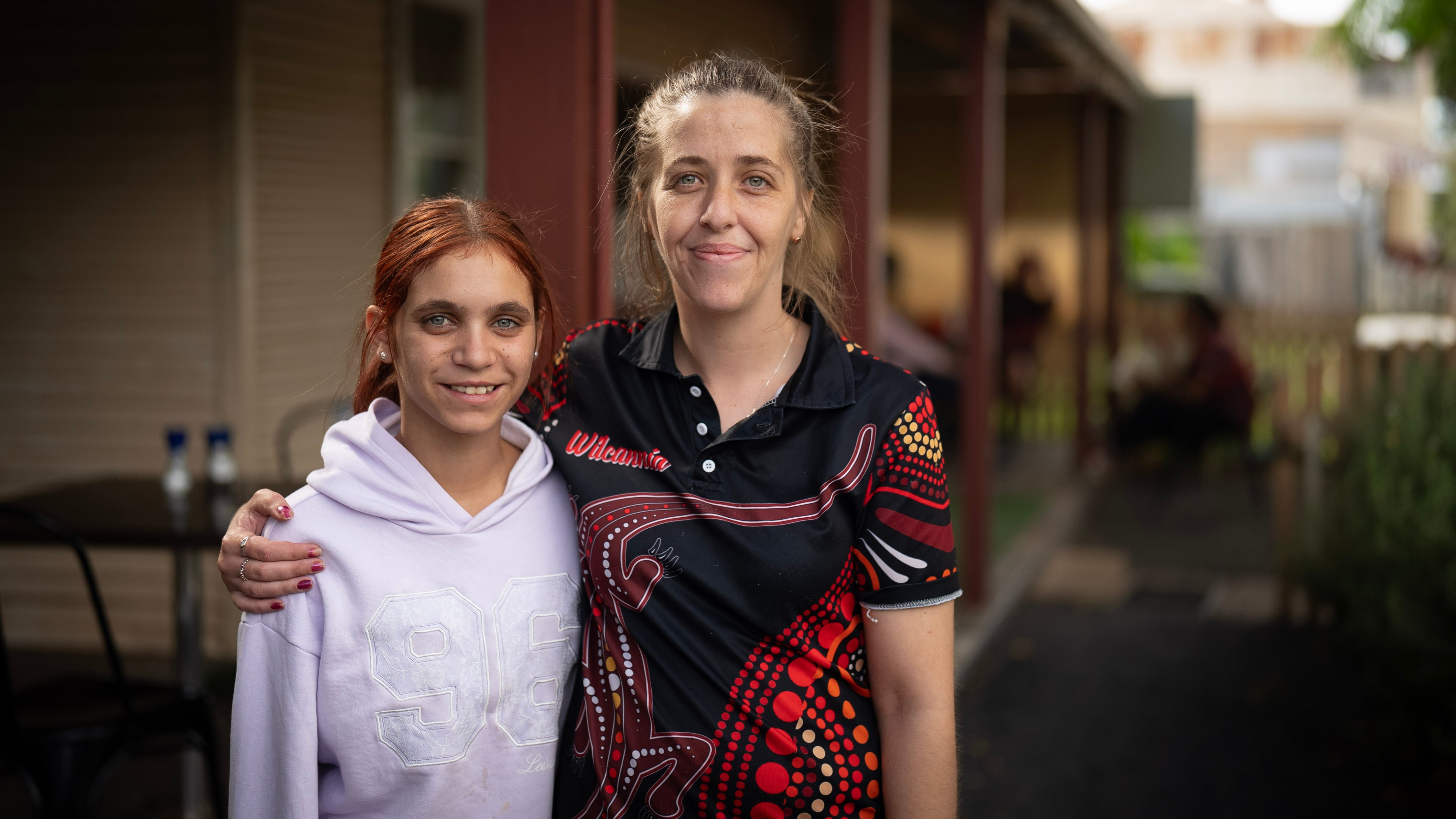 Two young women stand side by side smiling outside the Wilcannia cafe in outback nsw