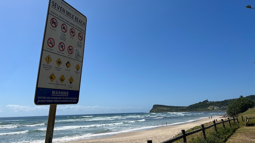A sign warning of dangers at Seven Mile Beach with Lennox headland in the background.