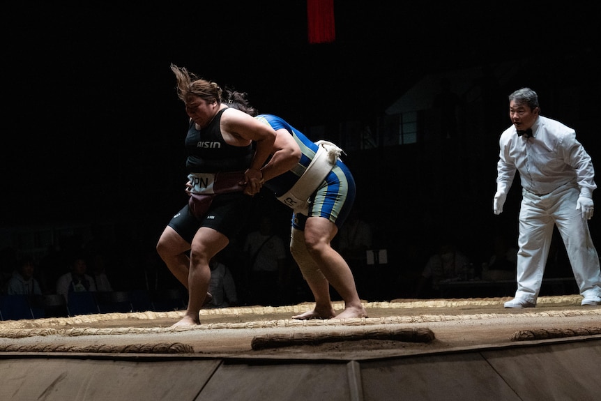 A woman shoves another woman out of a sumo ring