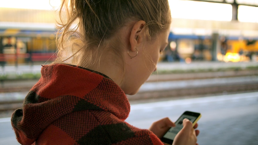 A woman at the train station in the evening checks her smartphone