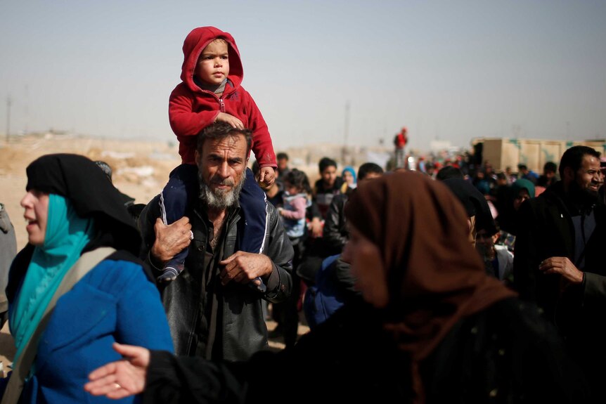 A boy on the shoulders of his father. People all around them.