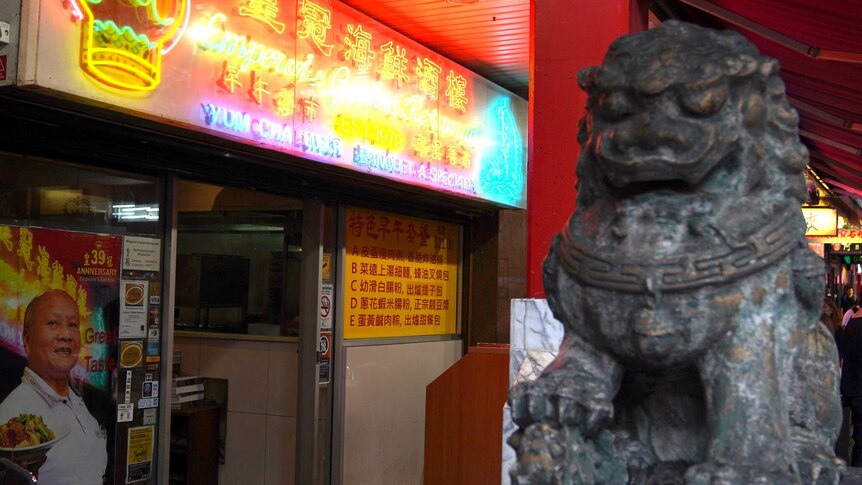 A large stone Chinese lion sits outside the restaurant, which has a bright neon sign and picture of Stanley Yee.