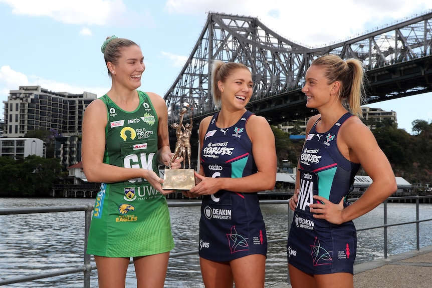 Captains hold the bronze Super Netball trophy as they stand in front of the Brisbane bridge