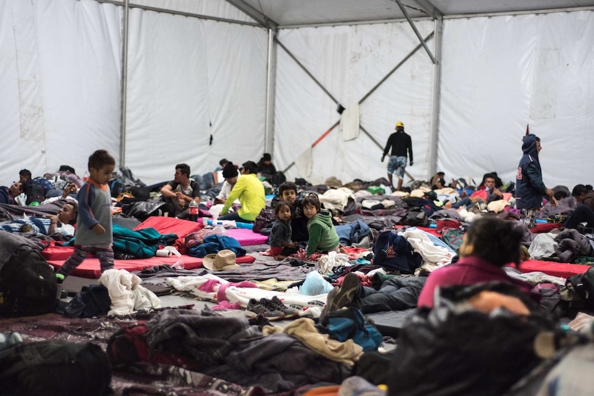 Children and young people from the migrant caravan gather on sleeping mats inside a dormitory tent