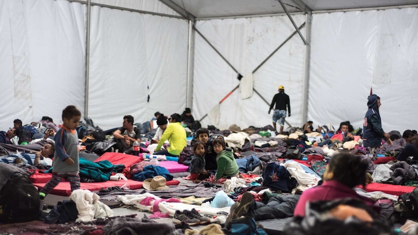 Children and young people from the migrant caravan gather on sleeping mats inside a dormitory tent