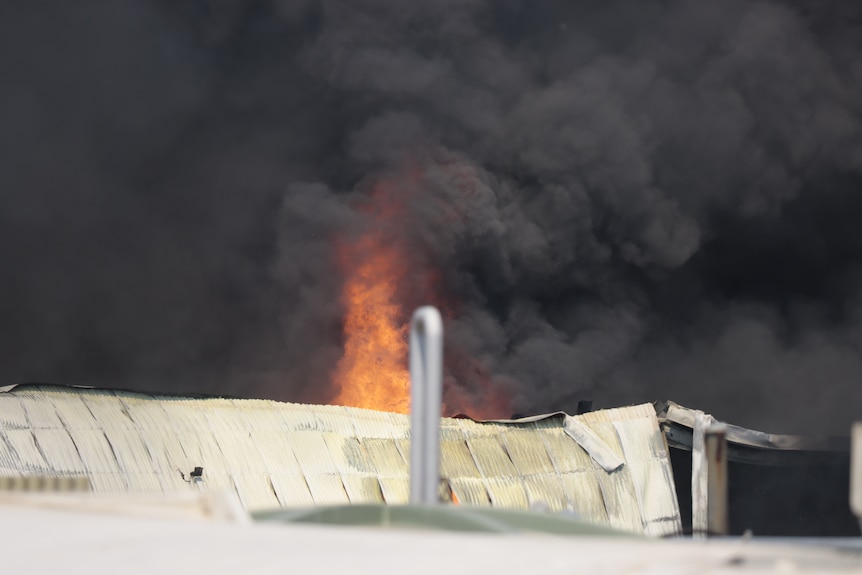 Se ven llamas sobre el techo de un edificio.  El cielo está negro con humo espeso. 