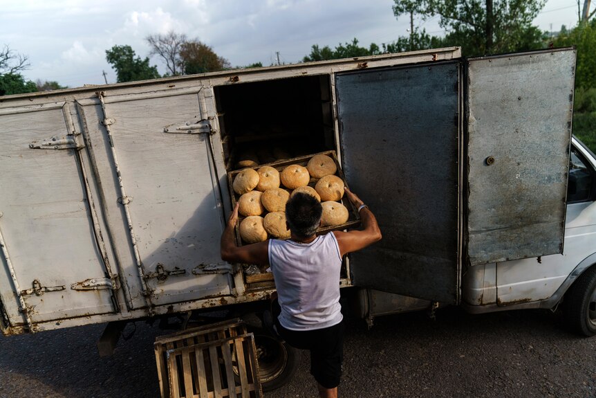 A man loading a tray of bread into a truck