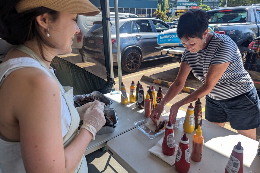 A woman serving up a sausge with sauce that she just bought.