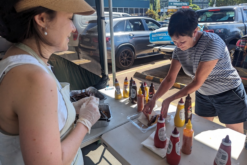 A woman serving up a sausge with sauce that she just bought.
