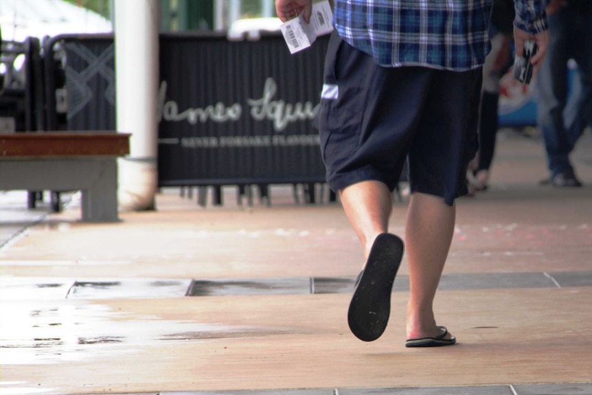 Man's legs pictured from the back as he walks down a wet path in Longreach.