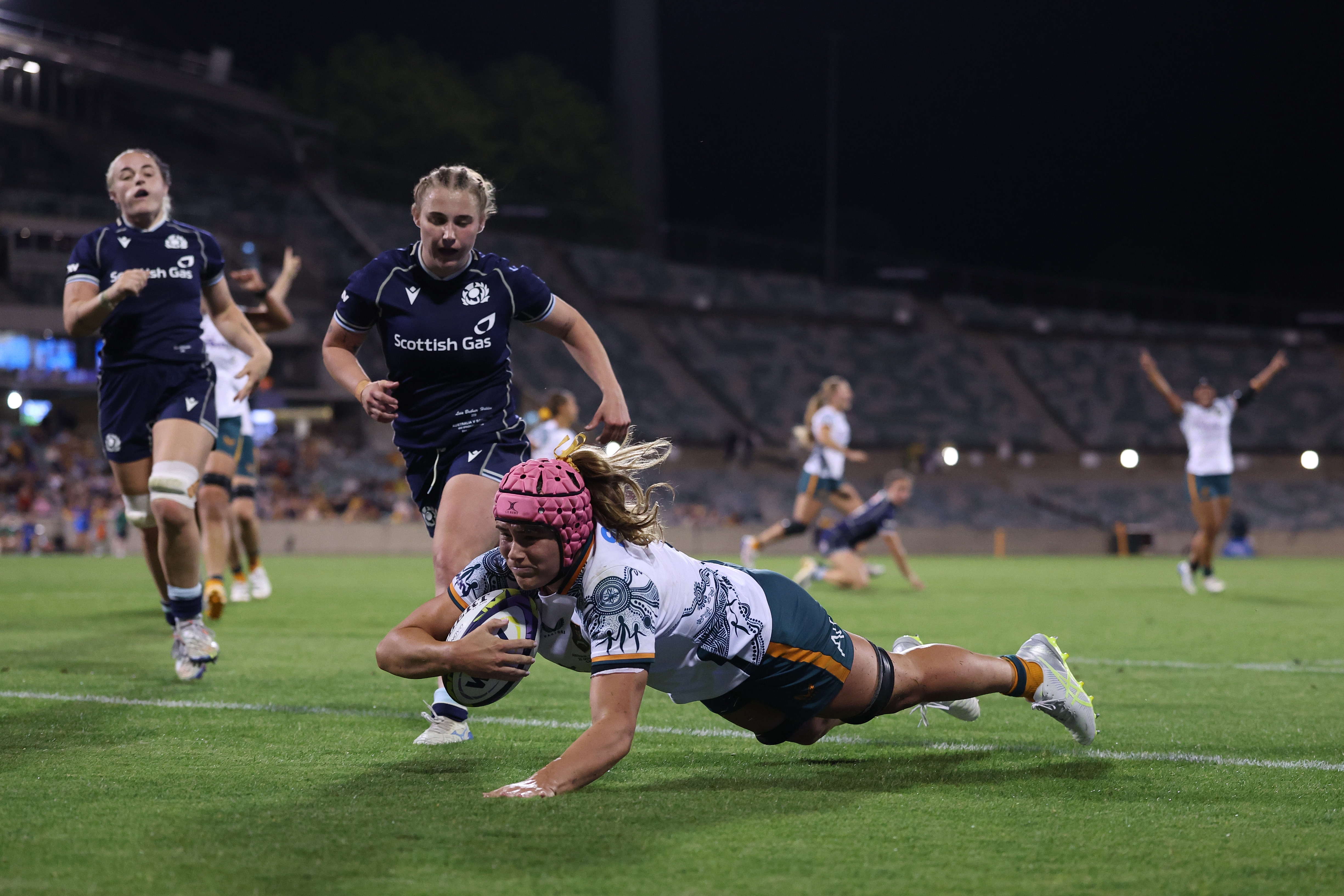 An Australian rugby player dives over to score a try as Scottish players chase and Australians celebrate in the background.