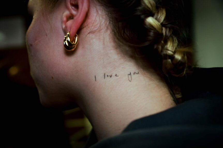 The words 'I love you' tattooed on the left side of the neck of a young queer woman