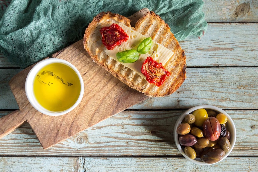 Piece of sourdough with cheese and tomatoes on a platter with olive oil and olives.