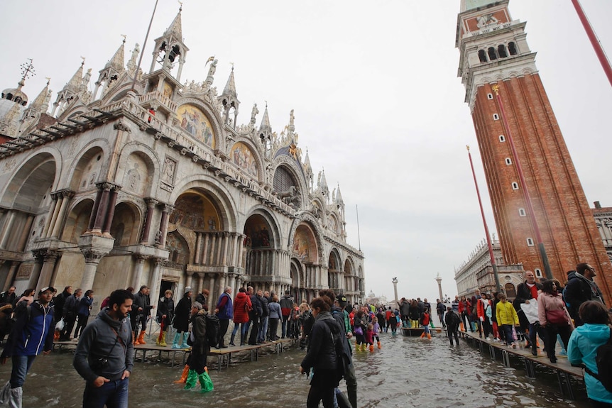 Hoards of tourists visit a flooded St Mark's Square on a cloudy day