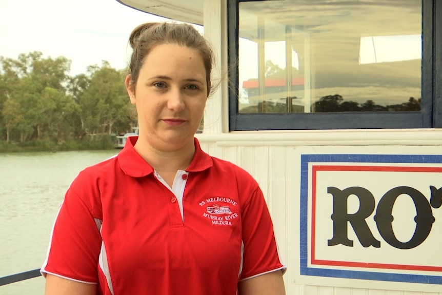 Ashton Kreuzer on the deck of a paddle vessel with gum trees and the Murray River visible in the background.