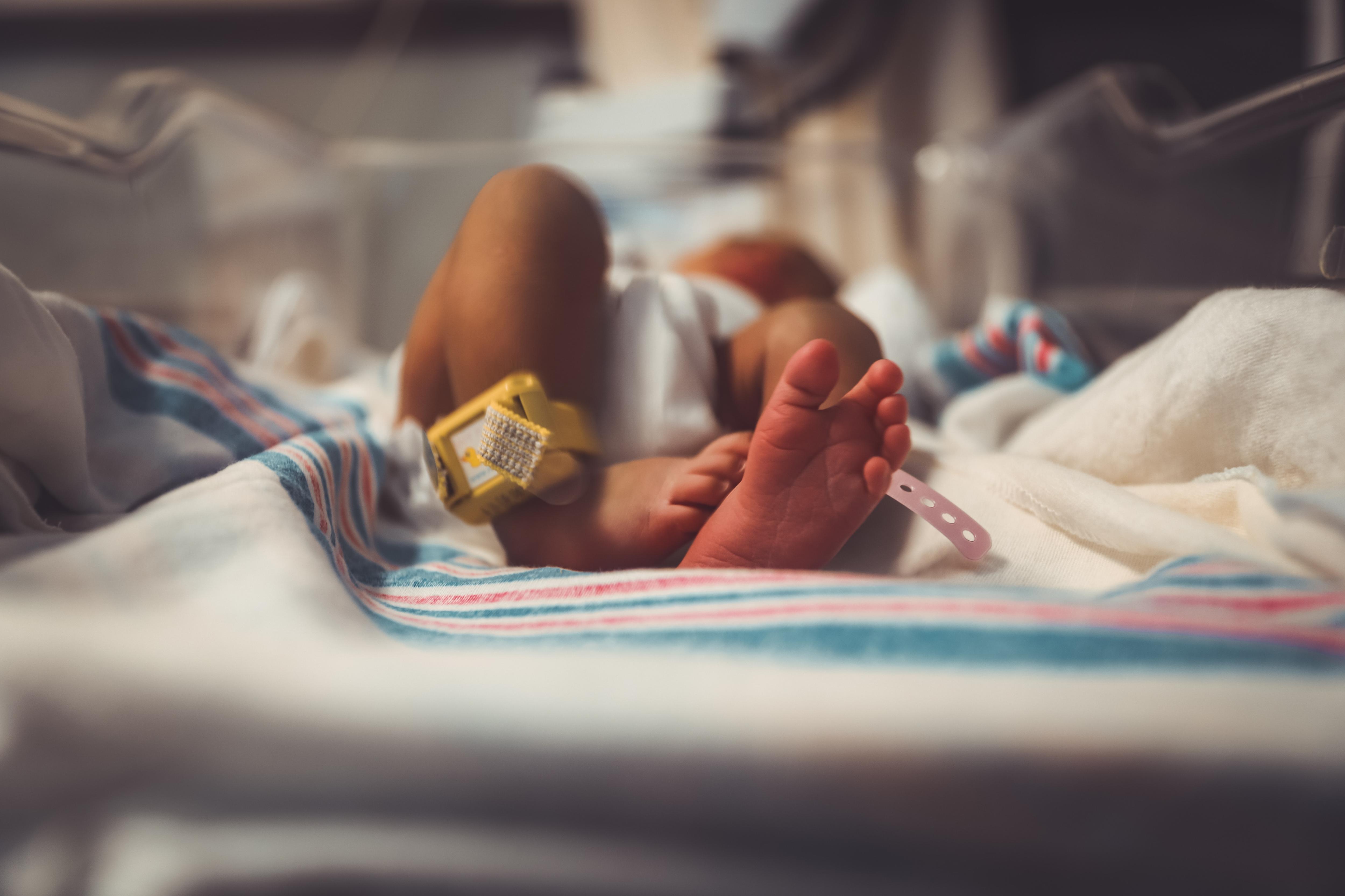 a photo of a newborn baby's foot lying in a hospital bassinet on top of a white, pink and blue hospital blanket