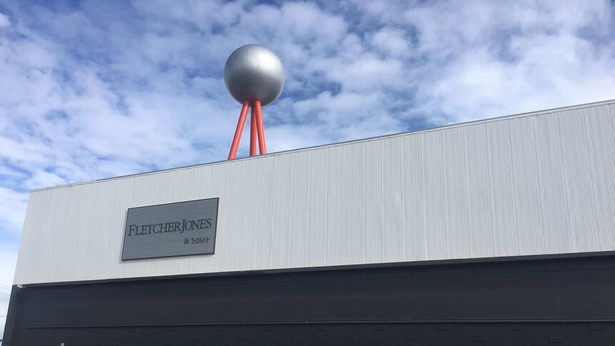 A view of the freshly repainted factory topped by a tripod and ball sculpture, signposted 'Fletcher Jones and Staff'