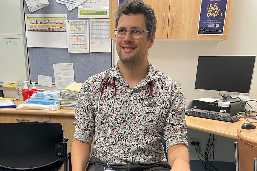 Dr Kenny sitting in a chair with one leg crossed over the other, smiling, wearing quirky socks.