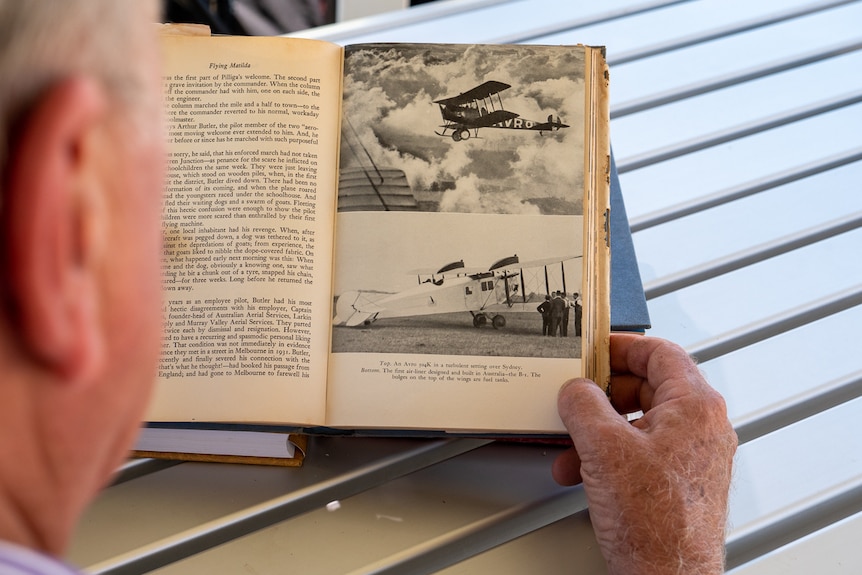 An over-the-shoulder shot of a man reading a book about aviation history.