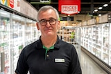 A man wearing a Woolworths polo shirt with the name tag 'Brad' stands in the cold food aisle of  supermarket.