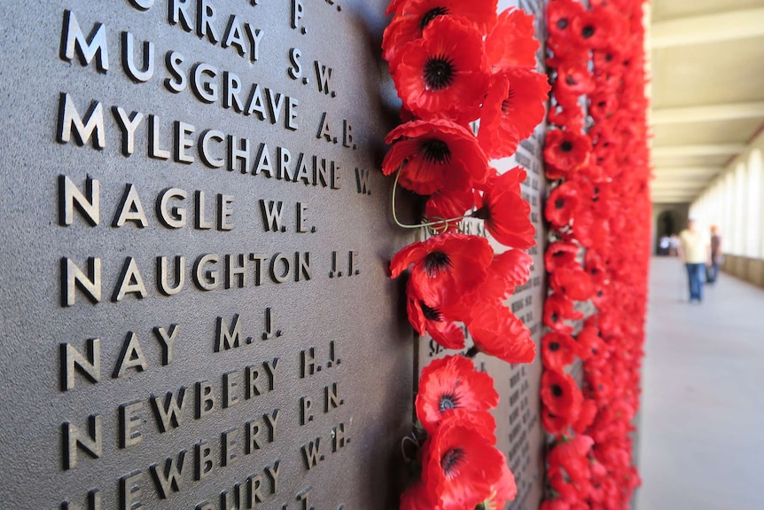 The name 'Naughton J.F.' in a list on a plaque at the Australian War Memorial, with red poppies placed next to it.