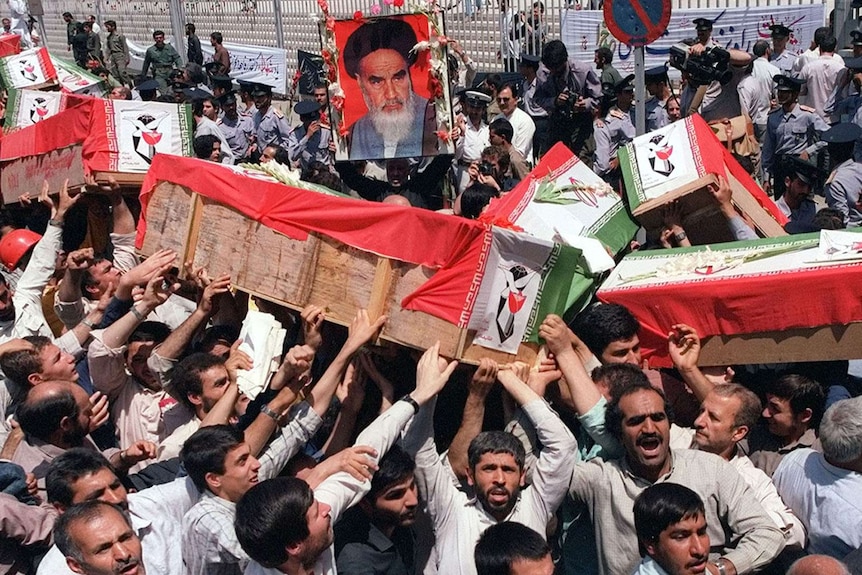 A crowd holds a number of caskets draped in the Iranian flag above their heads