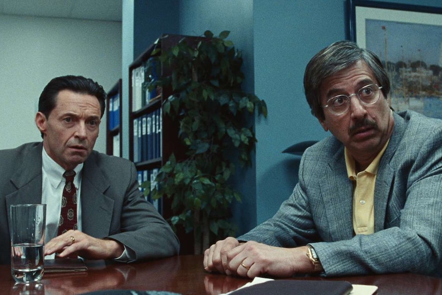 Hugh Jackman and Ray Romano in a scene from the film Bad Education - both stressed out in suits in an office