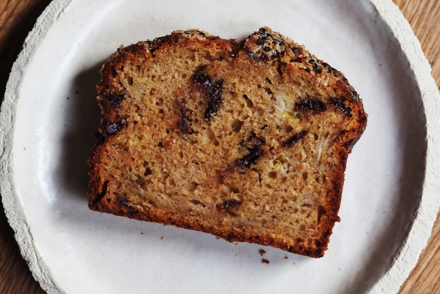 A slice of banana bread on a plate with chocolate, spices and a crunch tahini top: an easy banana bread recipe.