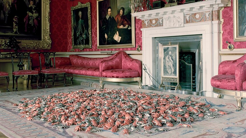 A large stately room with a fireplace and classical oil paintings host a contemporary installation of ceramic crabs.