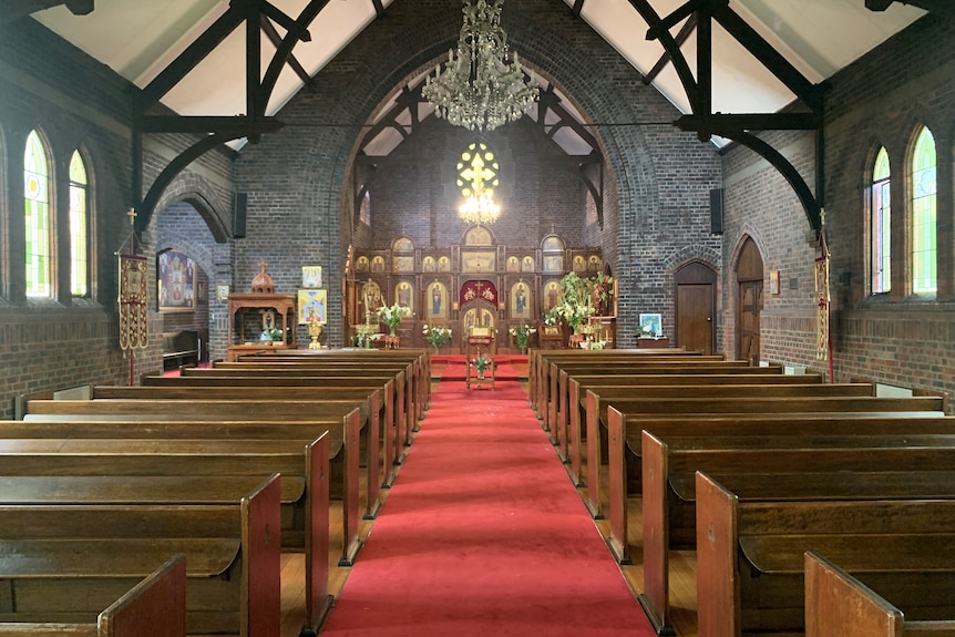 Red carpeted aisle of a church, with wooden seating on either side and ornate altar up front.