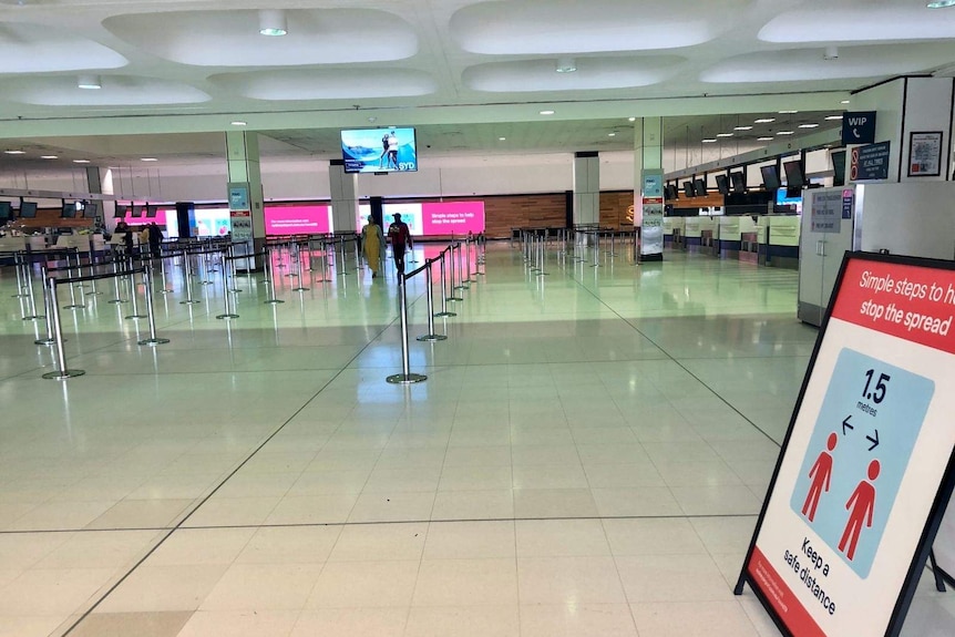 Airport walkways are empty with a sign in the foreground about social distancing