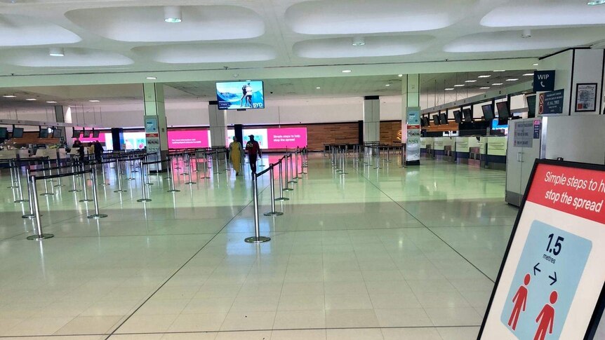Airport walkways are empty with a sign in the foreground about social distancing