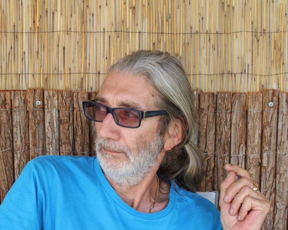 A man with glasses and his hair in a ponytail looks away from the camera.