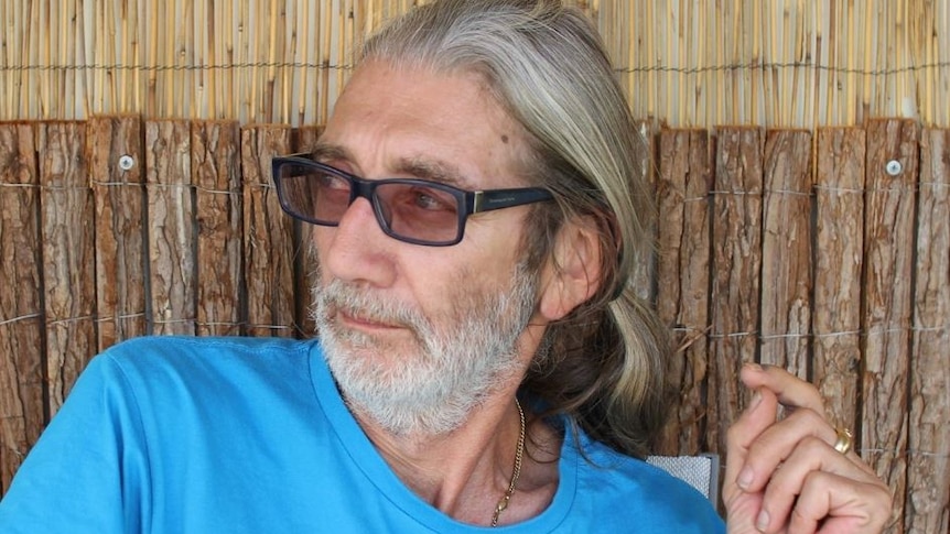 A man with glasses and his hair in a ponytail looks away from the camera.