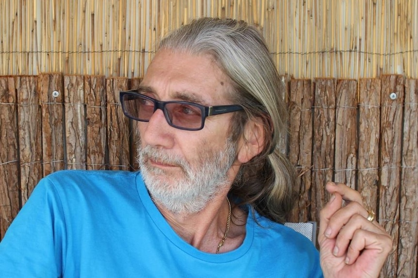 A man with glasses and his hair in a ponytail looks away from the camera.