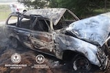 destroyed car burnt out among trees with police car in background