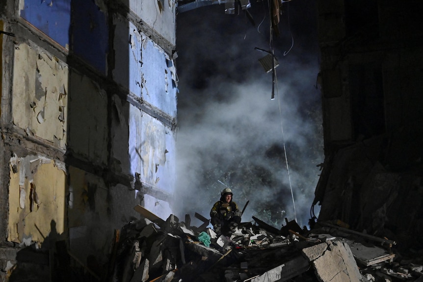 Un salvator se plimbă printre dărâmături lângă o clădire distrusă din Ucraina