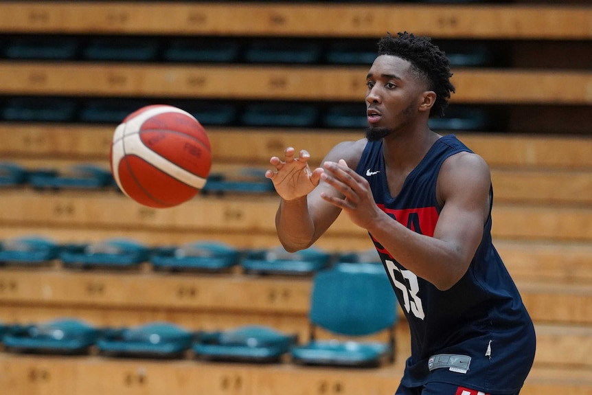 Donovan Mitchell shapes to catch a basketball that is flying towards him