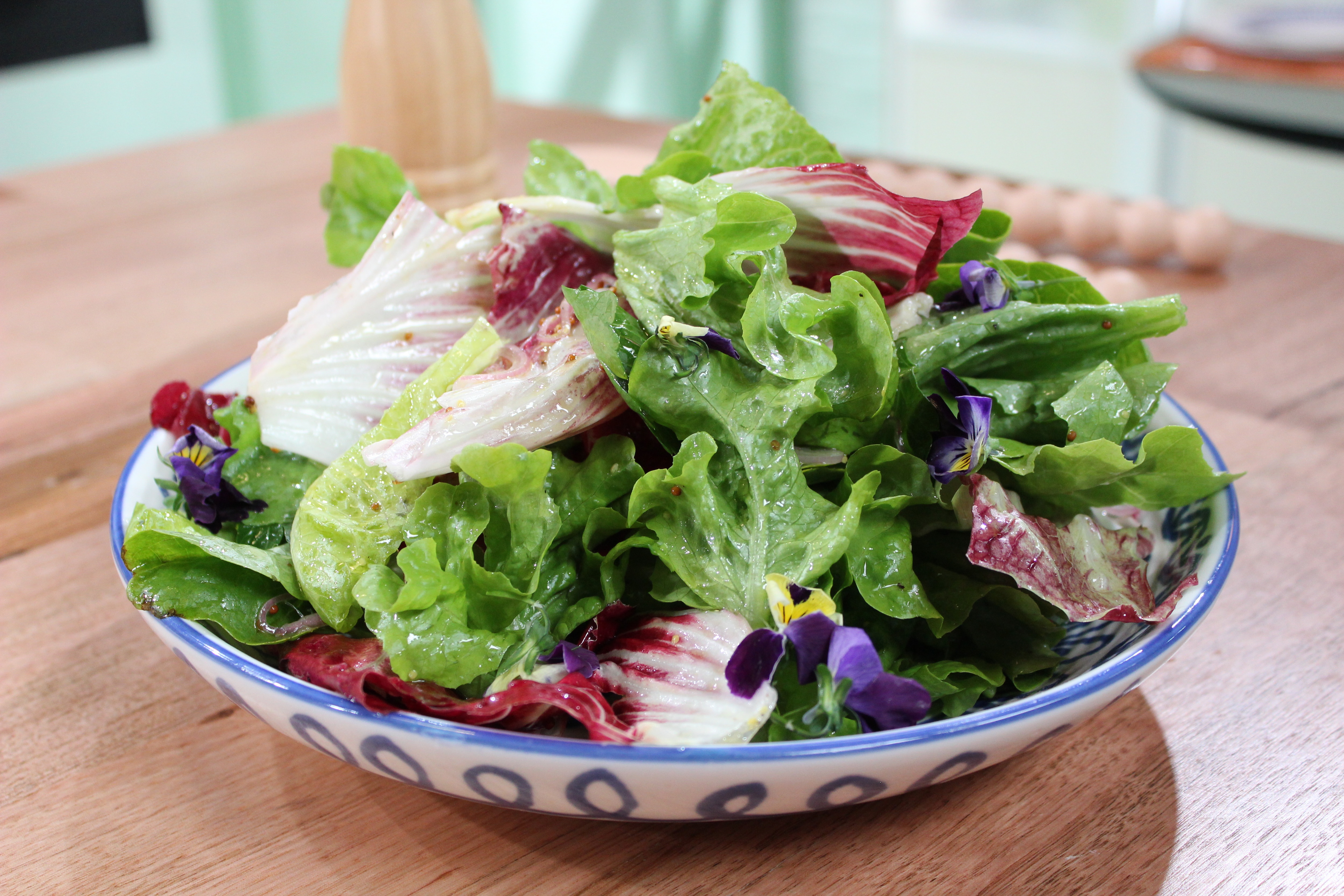 A picture of mixed lettuce leafs in a bowl garnished with seeded mustard vinaigrette.