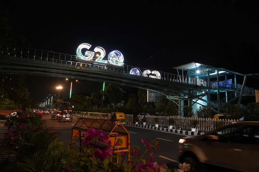 A G20 sign lit up at night over a major road with a bridge.