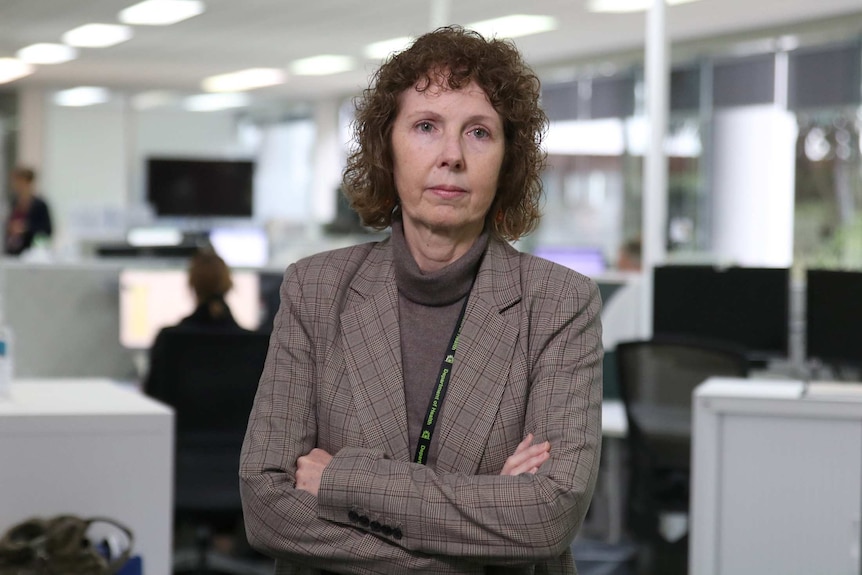 A mid-shot of Robyn Lawrence standing in an office with her arms folded looking serious.