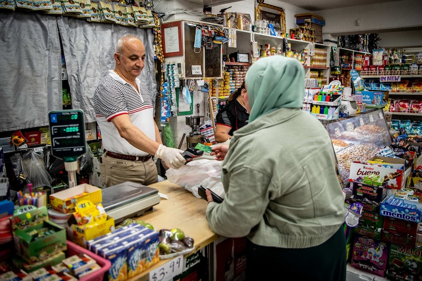 A man behind a shop counter holds an EFTPOS machine as a woman taps her credit card.