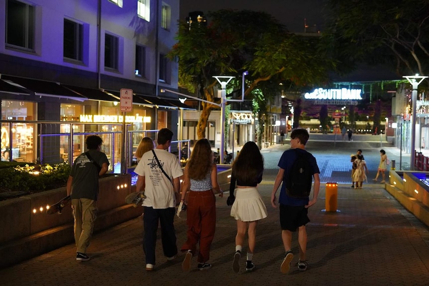 A group of young people walk around Southbank's restaurant precinct at night time.