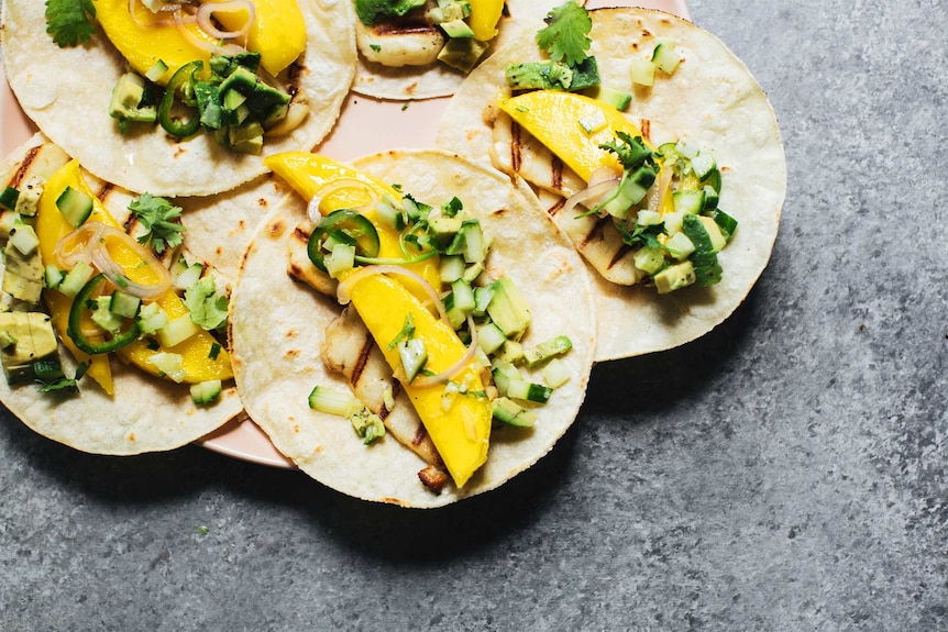 Soft tacos on a plate topped with haloumi, mango and cucumber avocado salsa for a quick summer recipe.
