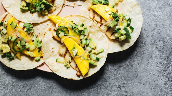 Soft tacos on a plate topped with haloumi, mango and cucumber avocado salsa.