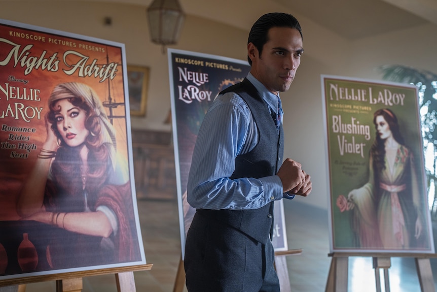 Diego Calva stands in front of 1920s movie posters in a still from the film Babylon