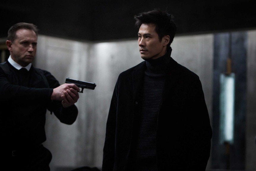 A scene from the movie The Translators with a man pointing a gun at another man